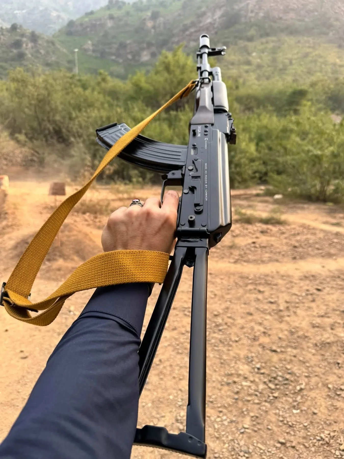 An AK-pattern rifle with a yellow sling, held outdoors