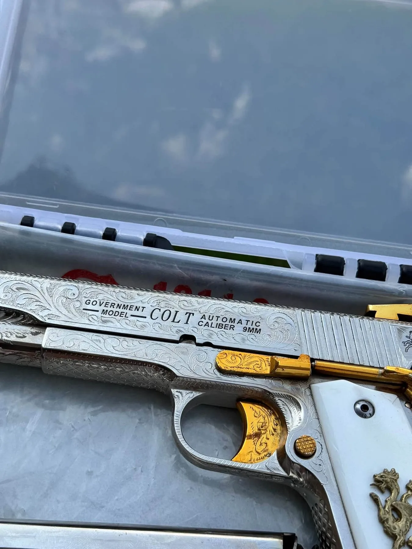 An engraved Colt 1911 pistol with gold accents in its case
